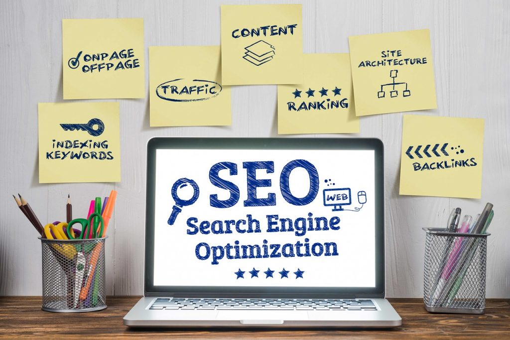 A laptop on a desk displays "SEO Search Engine Optimization" on its screen. Surrounding the laptop are sticky notes with terms like "Traffic," "Keywords," "Content," "Ranking," and "Site Architecture." The arrangement emphasizes the importance of organic traffic in digital marketing strategies.jpg