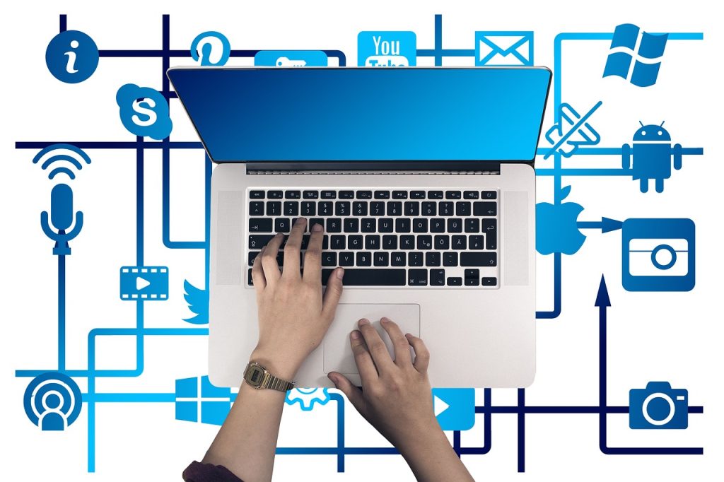 A top-down view image of hands typing on a laptop surrounded by various website and optimization icons such as a magnifying glass, gears, social media symbols, and cloud computing.