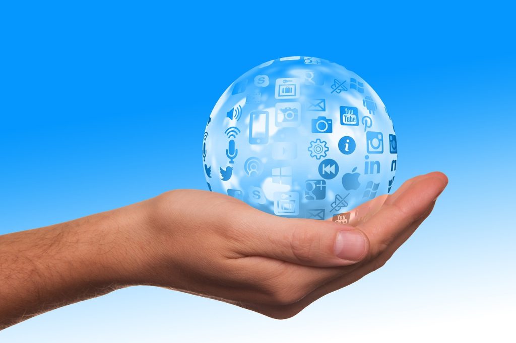 A hand holding a transparent sphere with various white icons related to technology and communication floating within it against a blue background